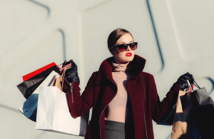 female with sunglasses, gloves and coat holding paper shopping bags in each hand
